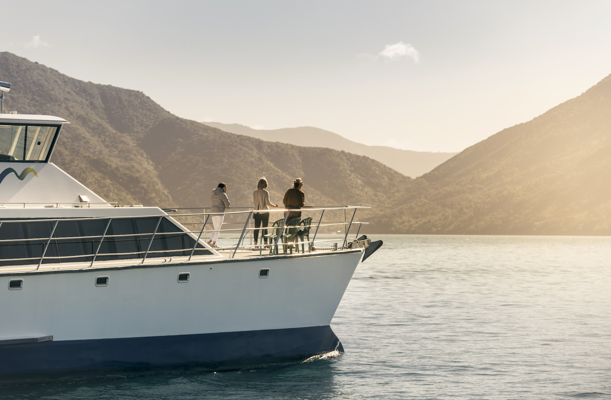 Cruising the Marlborough Sounds at the top of New Zealand's South Island, people view the sun set over the bush clad hills from the bow of MV Odyssea