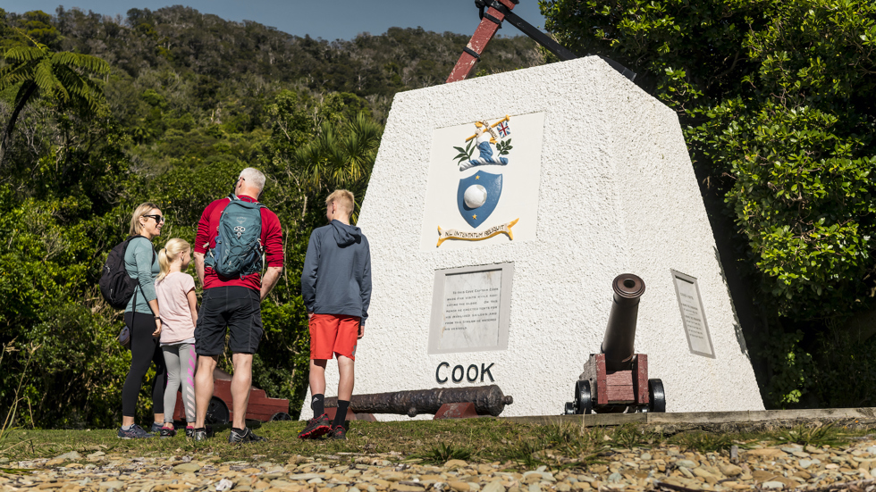 Family of four looking at the Captain Cook memorial at Ship Cove/Meretoto - the starting point of the Queen Charlotte Track.