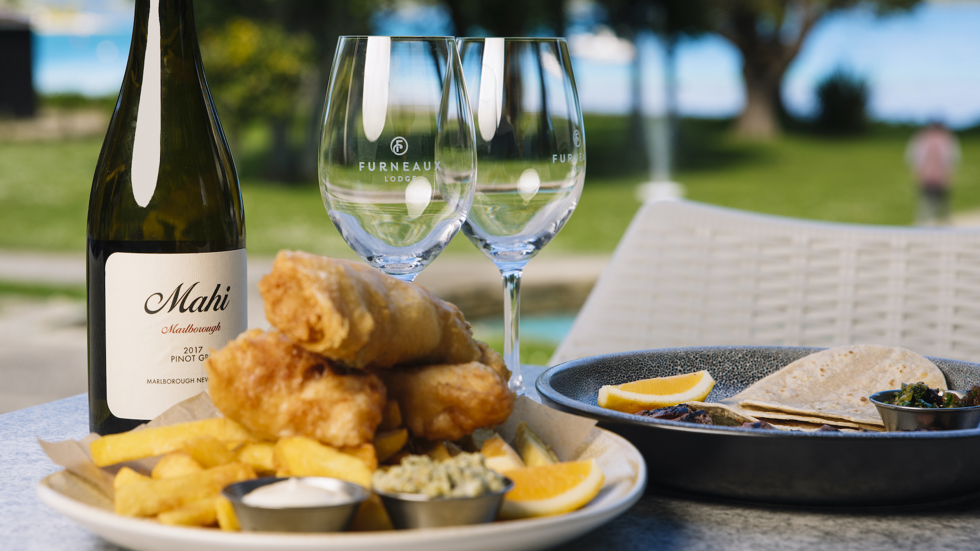 Furneaux Lodge's famous fish and chips with bottle of wine glasses and view of the water.