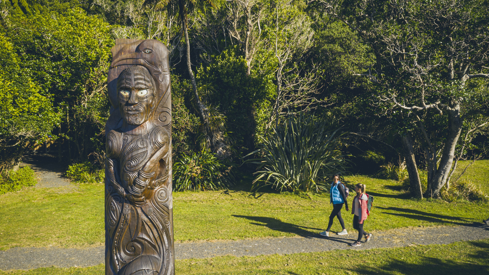 Pair of female walkers passing a Maori pou at Ship Cove/Meretoto - the starting point for the Queen Charlotte Track